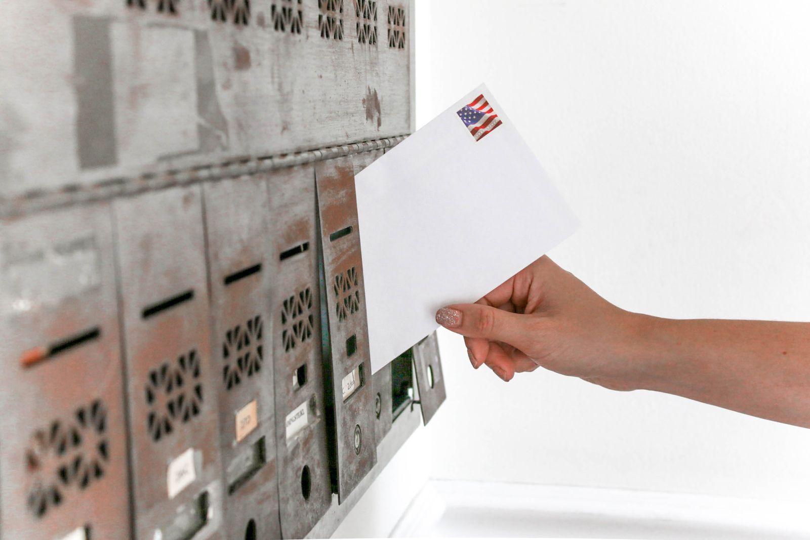 A hand slipping an envelope into an old bank of metal mailboxes