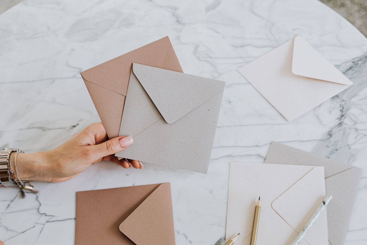 A hand holding craft envelopes over a marble table