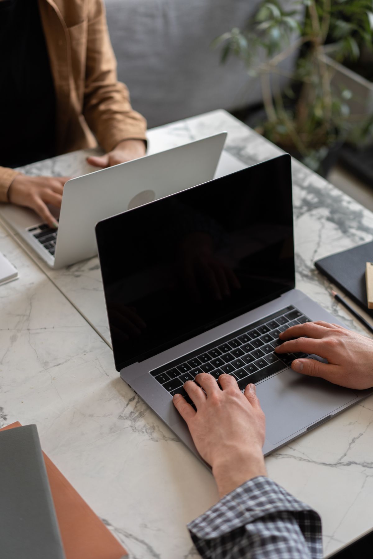 Two developers typing on laptops across a marble table